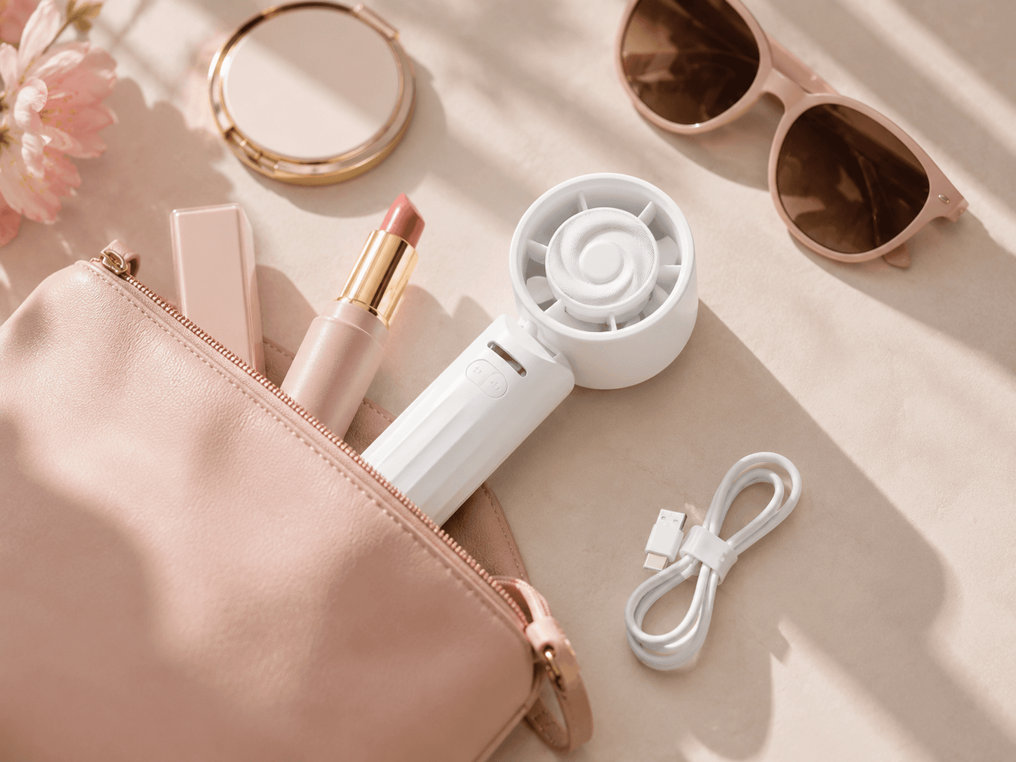 White handheld fan, pink lipstick, and sunglasses beside a makeup bag in warm sunlight.