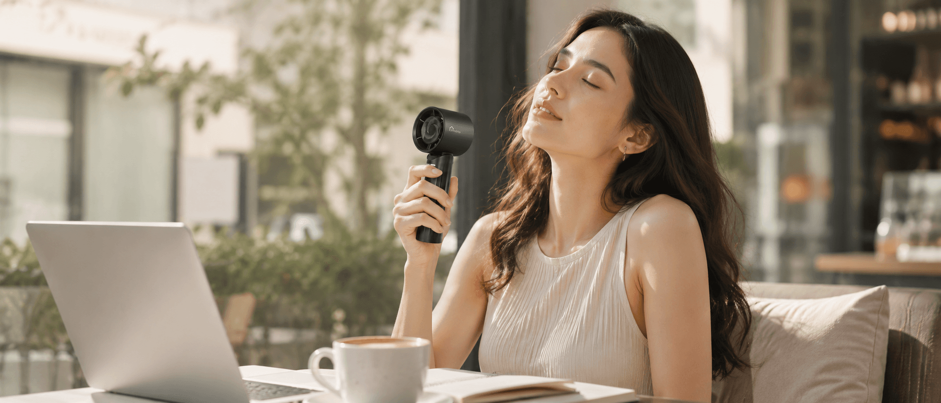 Woman at an outdoor cafe table using a small handheld fan to stay cool.